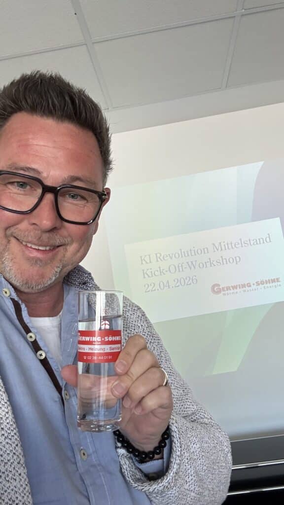 Ein Mann, der ein Marken-Glas in der Hand hält, vor einer auf eine Leinwand projizierten Werkstattpräsentation.